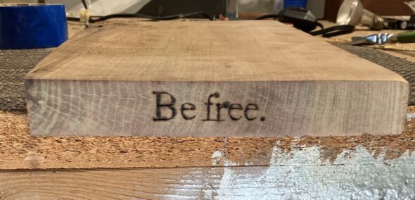 close up of wood burned shelf with text, "Be free."
